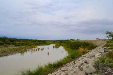 Küçük bir köprüsü ve bulutlu gökyüzü olan güzel bir göl manzarası.