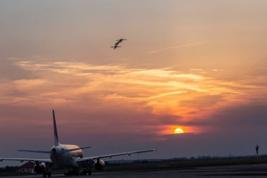 Two small planes doing acrobatics during sunset and a line airplane waiting on the runaway to take-off. Timisoara Air show or Aerotim Event on 15th of June 2019 on the Timisoara Traian Vuia Airport. clipart