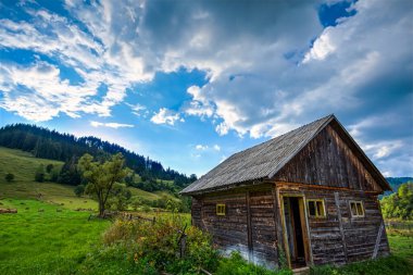 Eski, terk edilmiş ahşap kulübe güzel bir yaz günü mavi gökyüzü ve yeşil çimlerle görüldü. Fotoğraf 18 Ağustos 2020 'de Romanya' nın Harghita ilçesindeki Corbu köyünde çekildi..