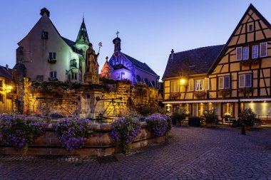 The main square of the feudal village of Eguisheim with half-timbered houses, an old fountain, and a church. Photo taken on 10th of August 2019 in the Eguisheim village, Alsace region of France. clipart