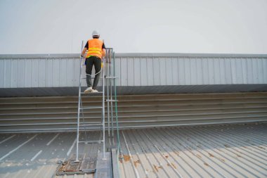 Beyaz kasketli ve koruyucu yelek giyen bir işçi işe gitmek için merdivene tırmanıyor..
