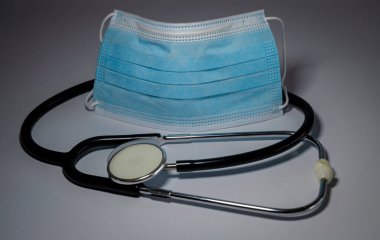 Üzerinde mavi cerrahi maske bulunan tıbbi steteskop gri arka plan, bakteri koruma konsepti, tıbbi ekipman konsepti.