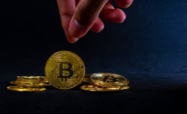 Altın Bitcoin, El, arka planda ışık huzmeleriyle birlikte yığının ortasında bitcoin toplamak üzere..