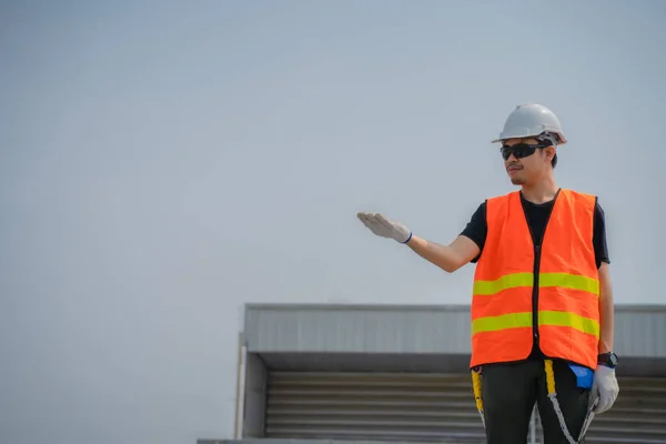 Asian engineers wearing protective vest and white hardhat standing with open hand and looking to the copy space while holding tablet.