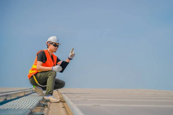 Asian engineer wearing protective vest and white hardhat sitting inspecting solar panel installation, Photovoltaic technology concept.