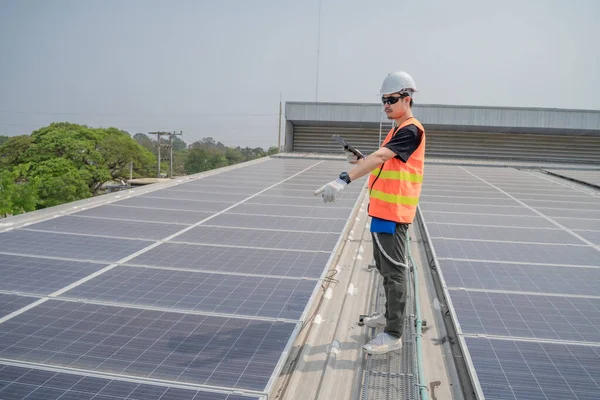 Asian engineers wearing protective vest and white hardhat standing using tablet and pointing to solar cell roof, Photovoltaic technology concept.