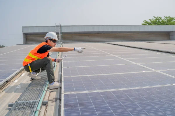 Asian engineer wearing protective vest and white hardhat pointing to the copy space on the solar panel roof, Photovoltaic technology concept.