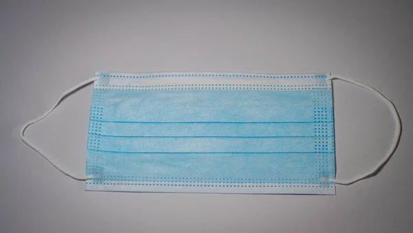 Blue surgical mask with rubber ears straps set in middle on gray background, Bacteria protection concept.
