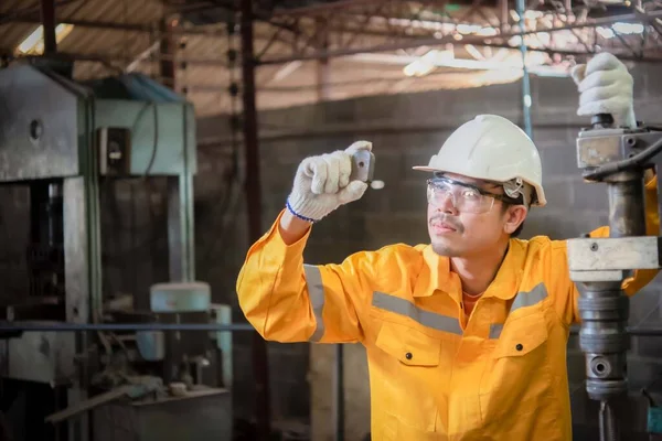 Engineer wearing yellow work clothes white hardhat and wear glove in close up shot holding material with drilling machine with serious face, Industry and production concept.
