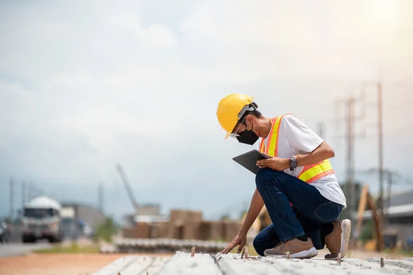 stock image Asian engineer wearing hard hat and safety vest sitting and checking construction problems in construction site.