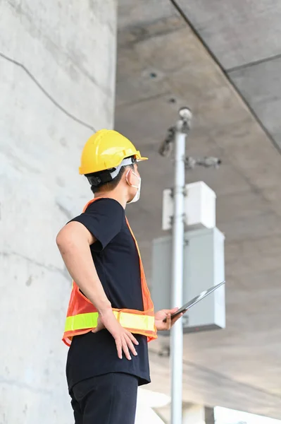 Asian construction worker wear hard hat and protection vest using tablet to check the place whether it is safe to work or not.
