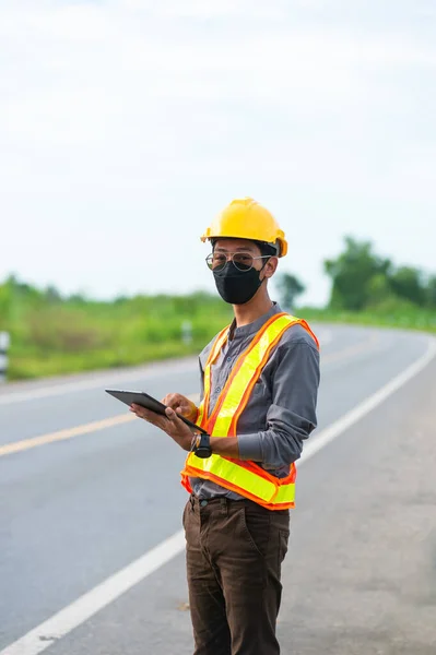 A young man wear a mask worker wearing protective wear using tablet standing on the street.