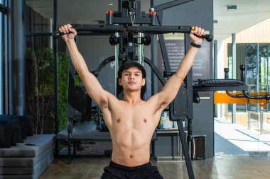 Asyalı yakışıklı adam vücut geliştirme merkezinde kollarına güç vermek için kol egzersizi makinesi kullanıyor..