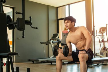 Asyalı yakışıklı adam spor salonunda kol kaslarını çalıştırmak için dambıl kullanıyor..
