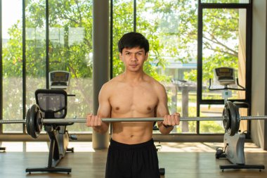 Asyalı adam spor salonunda halter kullanarak egzersiz yapıyor..
