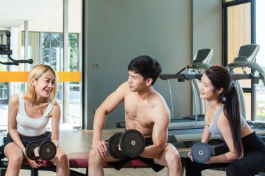 Yakışıklı genç antrenör spor salonunda iki çekici Asyalı kadınla dambıllarla egzersiz yapıyor..