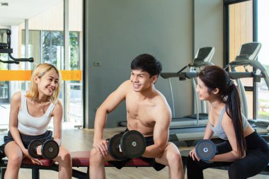 Yakışıklı genç antrenör spor salonunda iki güzel Asyalı kadınla birlikte spor yapıyor. Hepsi spor salonunda mutlu ifadeler takınıyorlar..