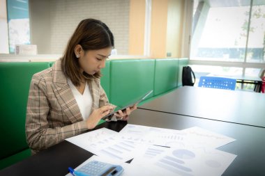 Güzel Asyalı iş kadını ofisinde oturmuş tablet bastırıyor..