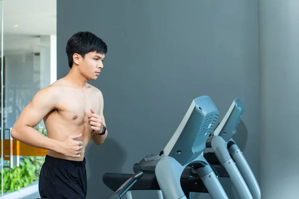 Asian handsome man good shape  muscle running on a treadmill for good leg strength at Fitness center.