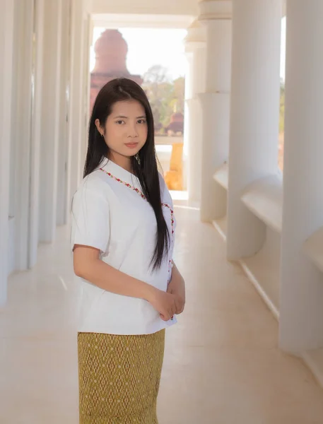 stock image Vertical picture of beautiful thai woman in a white traditional thai dress is standing in a white temple with a calm face.