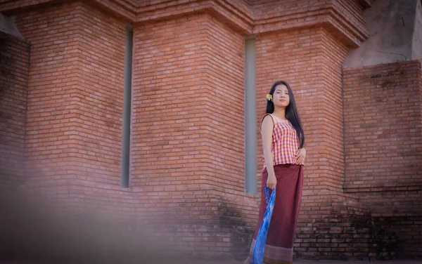 Beautiful thai woman in traditional thai dress is standing and holding a blue cloth iin an old temple with smile.