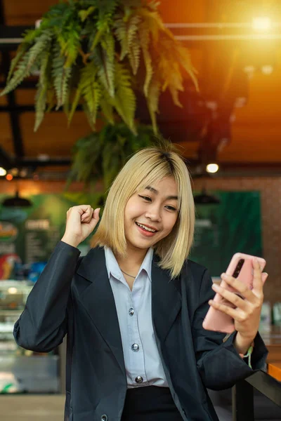 Asian beautiful business woman happy with good news on mobile phone in cafe.