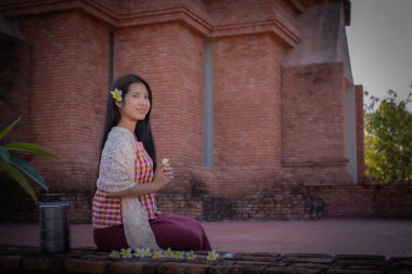 Taylandlı güzel bir kadın, geleneksel Tayland elbisesiyle omuzlarında beyaz bir bezle oturmuş, fotokopi odasına bakıyor elinde Frangipani çiçeğini tutarken yüzünde gülümsemeyle..