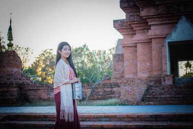 Akşamları güzel bir Taylandlı kadın geleneksel elbiseler giyer ve elinde eski bir tapınağın önünde yemek yerken ayakta durur..