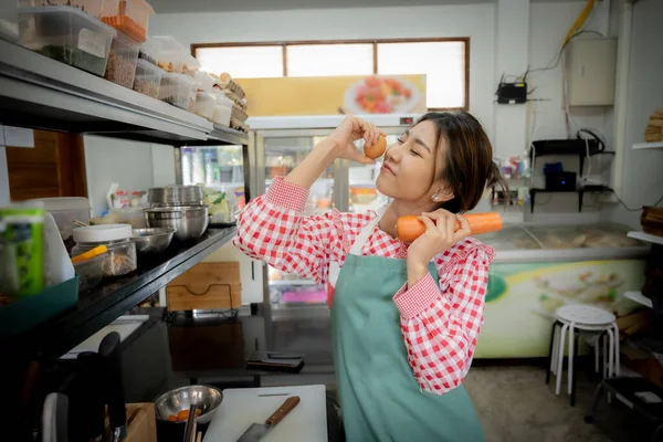 Beautiful asian female cook enjoying organic vegetables and carrots in kitchen background