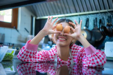 Güzel Asyalı çiftçi, yüzünde taze yumurtalarla mutfakta gülümsüyor..