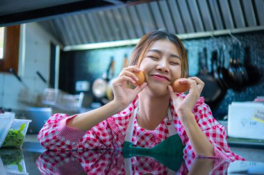 Güzel Asyalı çiftçi taze yumurtaları yanaklarında tutuyor. Mutfakta gülümseyen yüzüyle, Smart çiftliğinde..