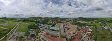 Güzel köyün panoramik manzarası ve arkasında yeşil tarlalar var. Mavi gökyüzü ve beyaz bulutları olan bir dağ..