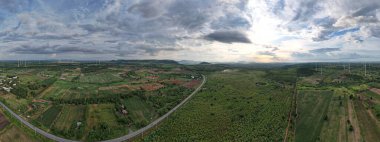 Yeşil orman ve güneş ışığı, yenilenebilir enerji ve çevresel koruma içeren kırsal ve yel değirmenlerinin panoramik görüntüsü.