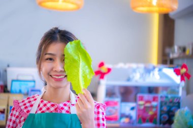 Önlük giyen güzel Asyalı çiftçinin yakın çekimi neşe dolu bir ifadeyle organik sebzeyi gösteriyor, Smart çiftliği..