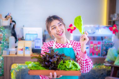 Güzel Asyalı garson önlük takıyor ve organik sebzelerle dolu bir tepsi gösteriyor. Bir yandan fotokopi alanına bakıyor, bir yandan Smart çiftliğine, hasat yapıyor..