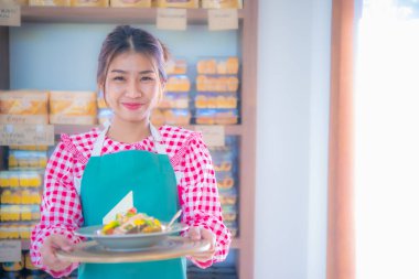 Güzel Asyalı garson elinde çeşitli organik sebzelerle dolu bir tabakla gururla gülümsüyor..