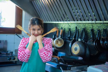 Güzel Asyalı aşçı önlük takıyor. İki eli de mutfakta kürek tutuyor. Kameraya bak..