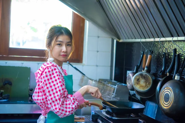 stock image Asian home cook woman holding spatula and pan cooking in the kitchen and looking to the camera indifferent expression, Healthy Food, Healthy Lifestyle, Seasoning.