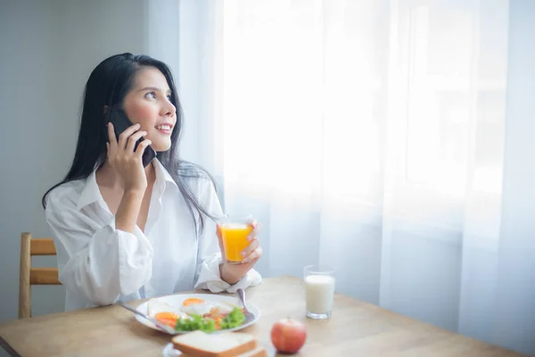 stock image Beautiful asian woman seemed completely at ease multitasking with ease and enjoying both her conversation and breakfast.