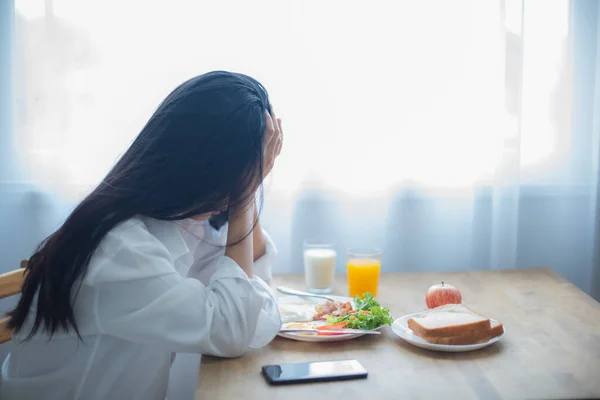 Beautiful asian woman sadness as she listened to the bad news on her phone while sitting down to eat breakfast.