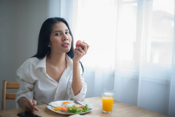 stock image Beautiful asian woman holding an apple and on the table having breakfast and a glass of juice.