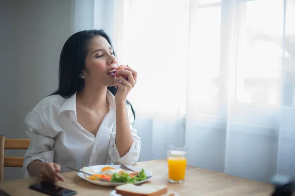 Beautiful asian woman eating an apple and on the table having breakfast and a glass of juice.