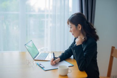 Asyalı güzel iş kadınının yan görünüşü endişeyle oturuyor iş detaylarını yüzünde gülümsemeyle yazıyor..