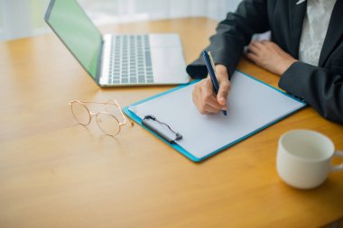 Elleri, yanında fotokopi alanı ve kahve fincanı olan önemli bilgileri belge ve dizüstü bilgisayara kaydediyor..