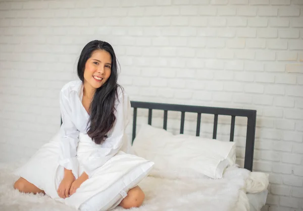 여자가 아침에 침대에 객실에 양손으로 베개를 카메라 앞에서 미소를 있습니다 — 스톡 사진