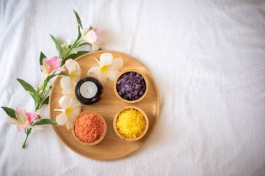 Bir kase portakal sarısı ve mor himalaya tuzu, rahatlatıcı ve lüks bir banyo için mükemmel beyaz bir plumeria taçyapraklarının yanında oturuyordu..