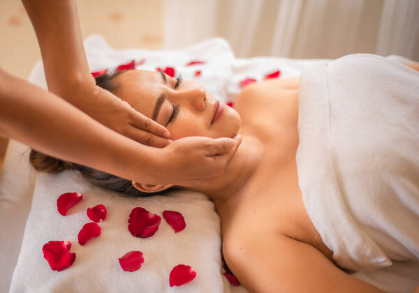 Beautiful asian woman lay on a bed strewn with rose petals the customer then closes her eyes and is comfortably massaged.