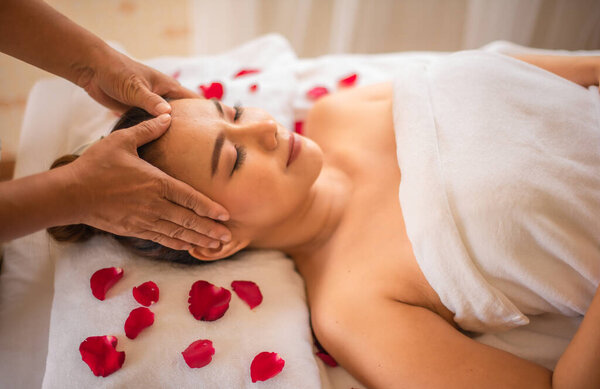 The expert masseuse gently kneaded the scalp of the beautiful asian customer with both hands on a bed strewn with rose petals.