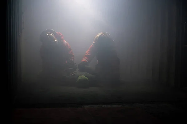 2人の消防士が暗い部屋で犠牲者のダミーを助けてる柔らかい光が差し込んでる — ストック写真