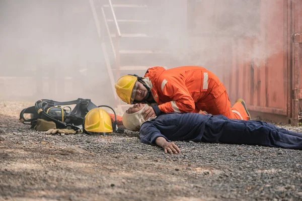 消防士は床に横たわっている犠牲者の脈拍と呼吸を確認するために傾斜し 人々を救う — ストック写真